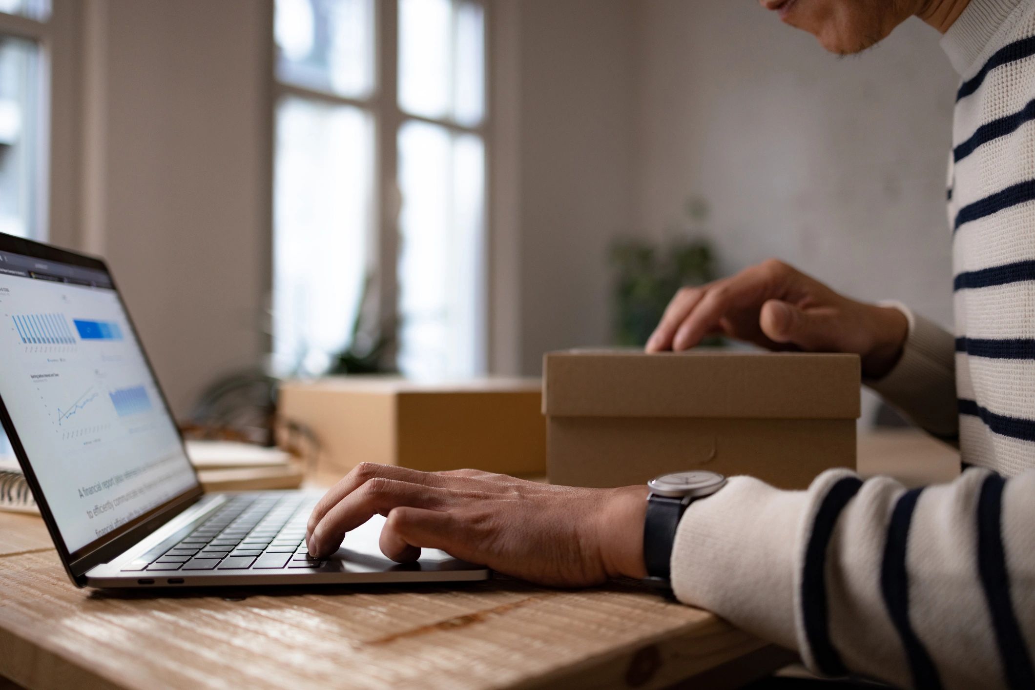 Small business owner preparing packages and paperwork at a laptop.